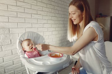 Anne küçük bebeği mutfakta besliyor.