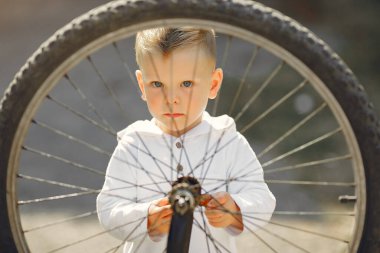 Küçük çocuk parkta bisikletini tamir ediyor.