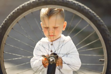 Küçük çocuk parkta bisikletini tamir ediyor.