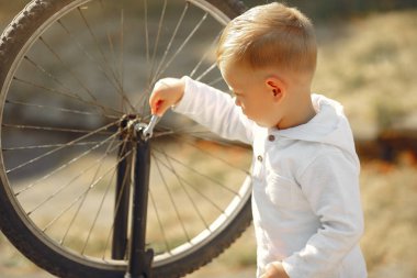 Küçük çocuk parkta bisikletini tamir ediyor.