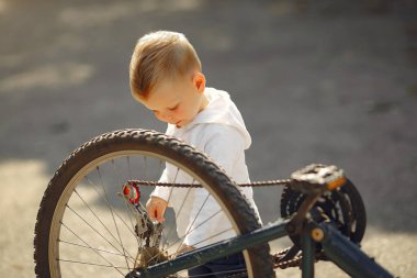 Küçük çocuk parkta bisikletini tamir ediyor.