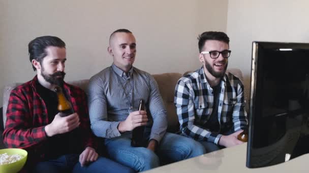 Três homens se sentam no sofá assistindo jogo de futebol — Vídeo de Stock