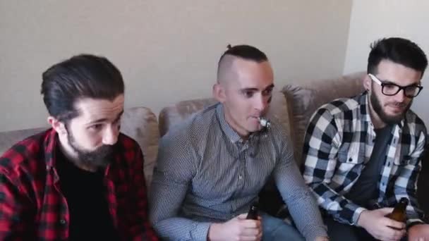 Três homens se sentam no sofá assistindo jogo de futebol — Vídeo de Stock