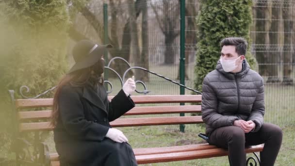 Lady and young man are sitting at the ends of a banch in a park — Stock Video