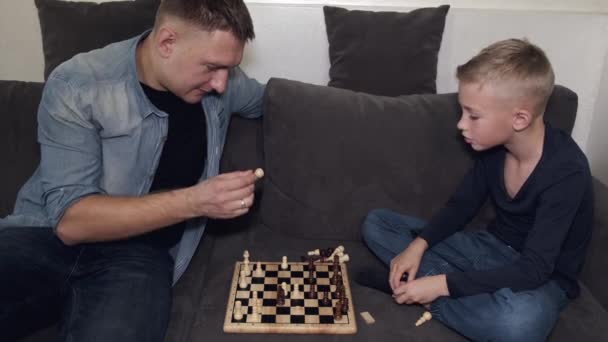 Vater und Sohn spielen zu Hause auf grauem Sofa Schach — Stockvideo