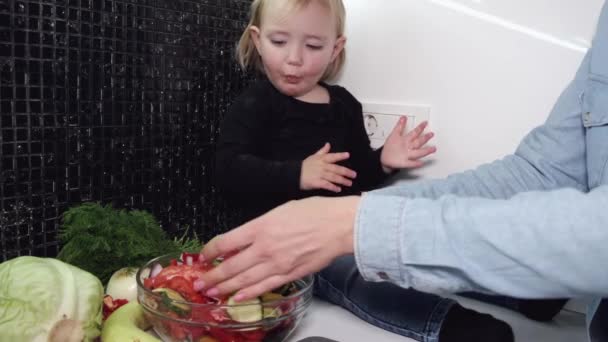 Little girl sits on table and observes cooking process — Stock Video