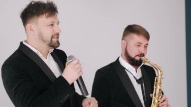 Siyah takım elbiseli iki adam stüdyoda şarkı söylüyor.