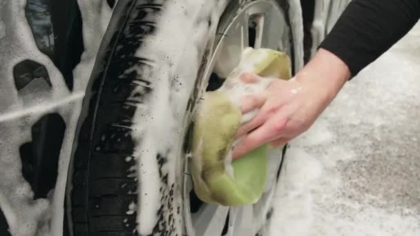 Adam arabasının tekerini süngerle yıkıyor. — Stok video