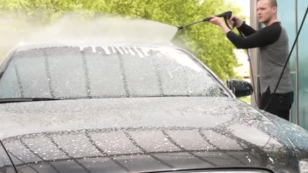 A fekete ruhás férfi vízipisztollyal mossa a kocsiját a szabadtéri önmosó pontnál. — Stock videók