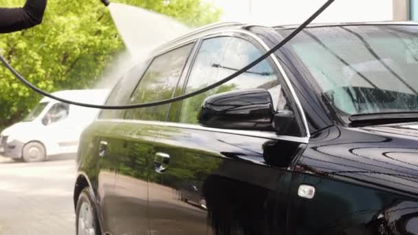 El hombre está enjuagando un coche negro en un punto de auto-lavado con la varita pulverizadora — Vídeos de Stock