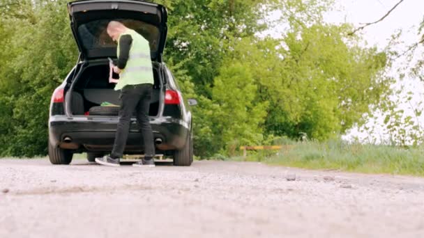 A fényvisszaverő kabátos sofőr beállítja a figyelmeztető háromszöget az autó közelében. — Stock videók