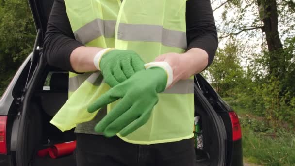 Mannen i en reflekterande jacka sätter på handskarna framför en bil. — Stockvideo