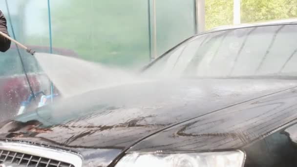 Mannen sköljer en svart bil vid en självtvättande bilpunkt med stänkstaven — Stockvideo