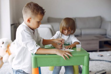 Çocuklar yeşil masada oturuyor ve resim çiziyor.