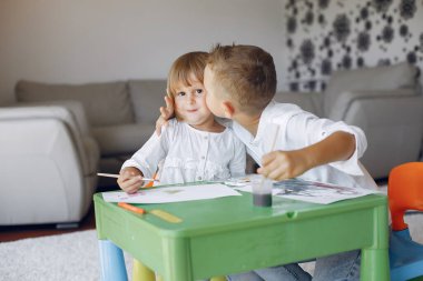 Çocuklar yeşil masada oturuyor ve resim çiziyor.