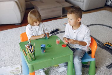 Çocuklar yeşil masada oturuyor ve resim çiziyor.