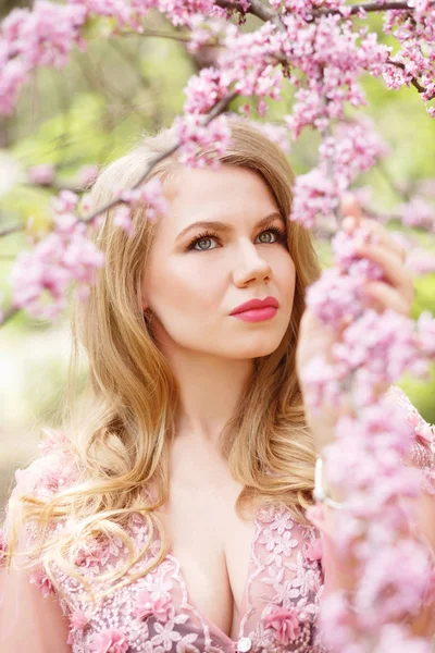 Hermosa mujer de ojos verdes sosteniendo una rama de cerezo en flor en las manos . Imagen De Stock