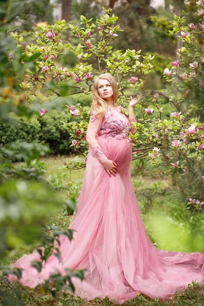 Madre embarazada en sexy hermoso vestido largo en el jardín cerca de magnolia floreciente — Foto de Stock