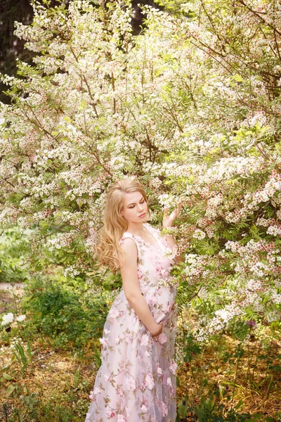 Joven embarazada womani n floral vestido rosa de pie los árboles con flores Imágenes De Stock Sin Royalties Gratis