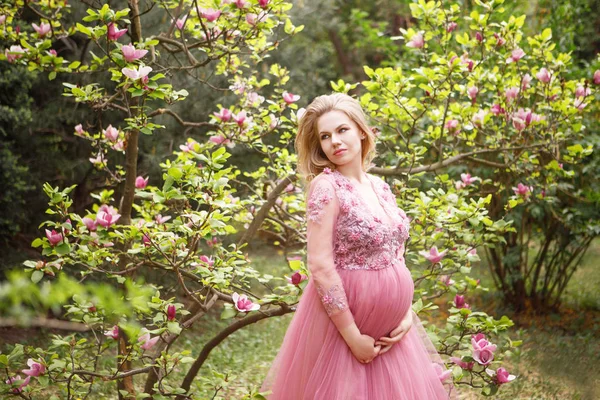 Mujer encantadora esperando bebé en hermoso vestido fondo de magnolia floreciente y vegetación Imagen De Stock