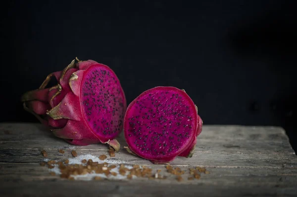 Red Dragon fruit on wooden surface, solid black background, still life shooting style.