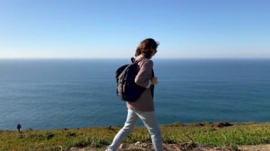 Genç bir kadın kamera bir yol boyunca uzak bir tepenin arka plan mavi okyanusun üzerinde yürür. Bir sırt çantası bir kızla etrafında döner, kamera ve gülümsüyor görünüyor.