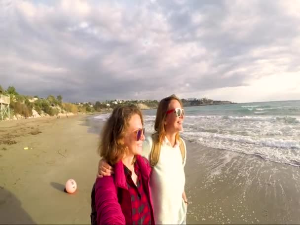 Dos mujeres jóvenes están caminando por la costa riendo hablando y besándose . — Vídeo de stock