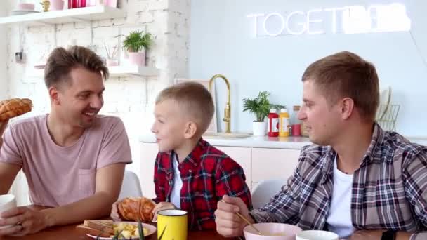 Gelukkig gay familie twee vaders en zoon zitten ontbijten in de keuken. — Stockvideo