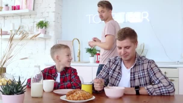 Happy gay familie to fædre og søn spiser morgenmad i køkkenet . – Stock-video