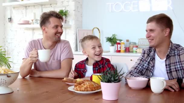 Happy gay family two fathers and son are having breakfast in the kitchen. — ストック動画