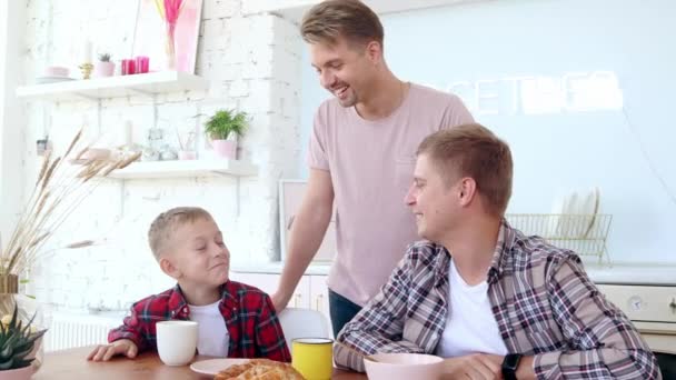 Gelukkig gay familie twee vaders en zoon zitten ontbijten in de keuken. — Stockvideo