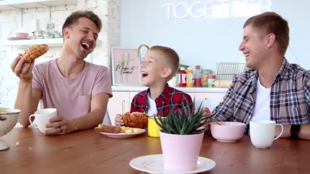 Feliz gay família dois pais e filho são tendo pequeno-almoço no o cozinha . — Vídeo de Stock