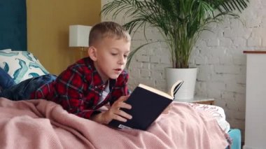 Sekiz yaşında bir çocuk yatağa uzanıp kitap okuyor..