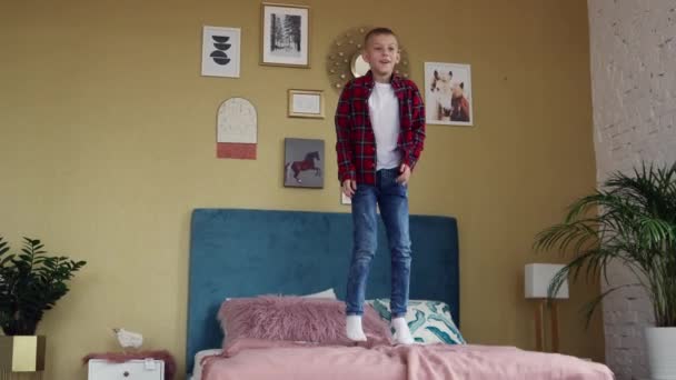 Un joven de ocho años saltando alegremente sobre la cama de los padres . — Vídeos de Stock