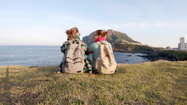 Två unga kvinna backpackers sitter vid kanten av en klippa — Stockvideo