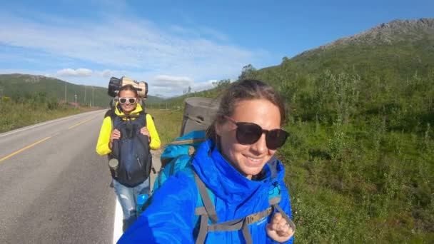 Dvě mladé ženy cestují bloggerů chůzi norské silnici a přičemž selfie. — Stock video