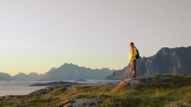 Kadın gezgin bir tepeden Norveç manzarasının keyfini çıkarıyor ve dinleniyor.