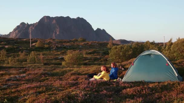 Két fiatal nő ül a turista sátor mellett, kilátással a fjordra. — Stock videók