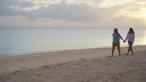 Two young happy women walking on the beach at the sunset time. — Stock Video