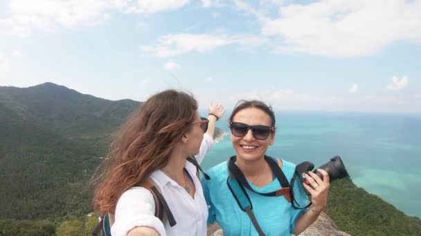 Duas jovens mulheres de pé na colina com vista para o mar e tirar uma selfie — Vídeo de Stock