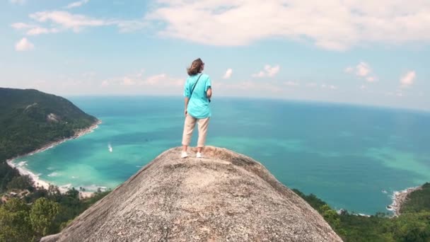 A young woman standing at the edge of the rock with a sea view. — Stockvideo