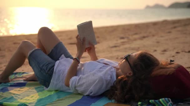 Una giovane donna che legge un libro e si rilassa sulla spiaggia — Video Stock