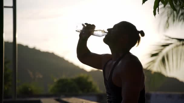 Hombre atlético bebiendo agua de una botella en un gimnasio al aire libre . — Vídeos de Stock