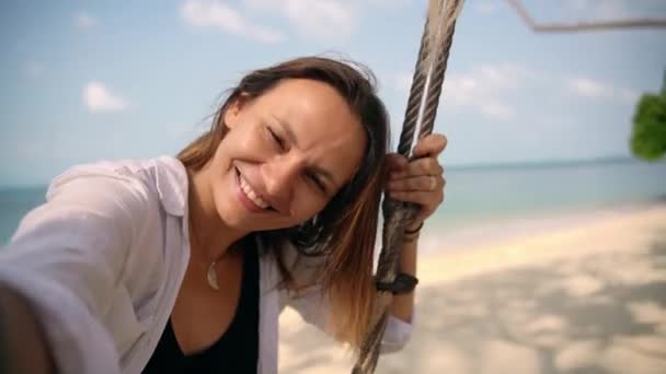 Μια νεαρή γυναίκα βγάζει μια σέλφι ενώ αιωρείται σε μια κούνια στην παραλία — Αρχείο Βίντεο