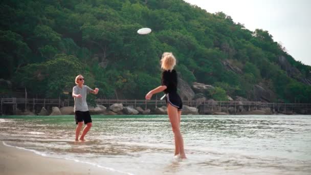 Dos jóvenes lanzando un frisbee en la playa tropical en un día soleado . — Vídeos de Stock