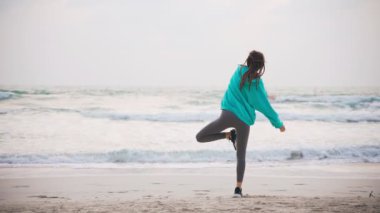 Young woman trying to do yoga at the beach at the sunrise time. 