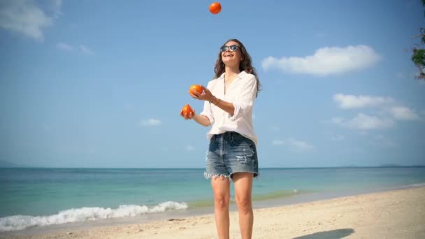 Jonge vrolijke vrouw jonglert mandarijnen op het strand op een zonnige dag. — Stockvideo