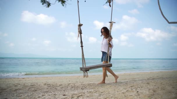 Une jeune femme vient à une balançoire sur la plage et commence à balancer . — Video