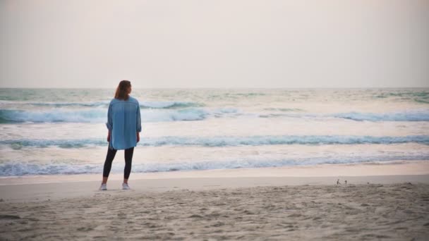 Kobieta stoi na plaży i podziwia widok na morze. — Wideo stockowe