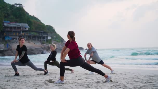 Группа из четырех молодых женщин, занимающихся разминкой на пляже на рассвете . — стоковое видео